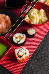 Sushi rolls, ginger and wasabi on red mat and black table
