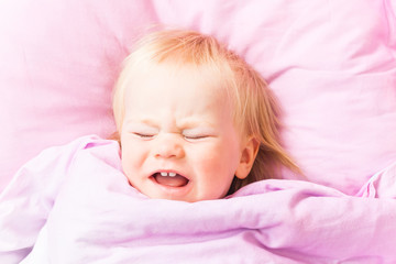 An awakened baby in a bed on a pink cushion