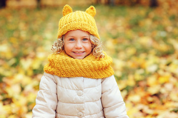 funny autumn portrait of happy toddler girl walking outdoor in stylish knitted orange snood