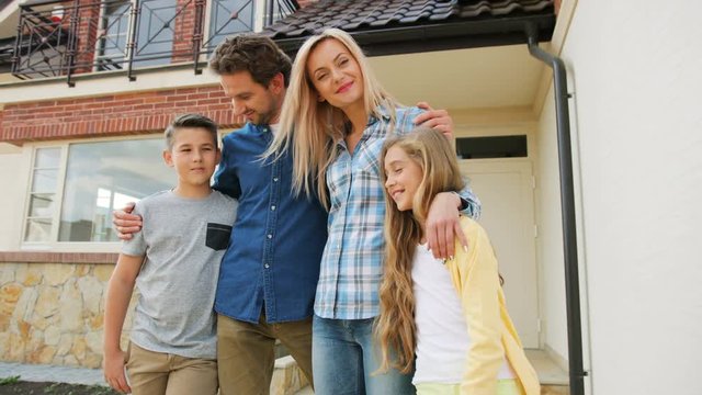 Portrait of happy caucasian family in front of new home, hugging and smiling on camera.