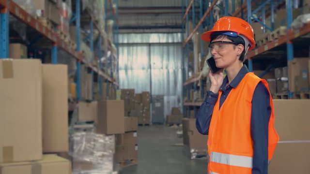 woman worker in storehouse using wireless barcode scanner scanning labels on boxes before delivery in logistic center. professional employee wearing uniform high visibility orange hard hat and vest