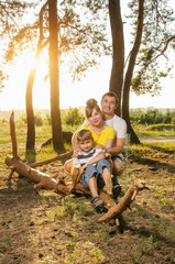 Naklejka na ściany i meble Happy family, walking in the fresh air, the parents sitting on a log with his child