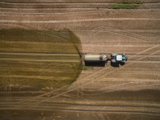 Naklejka premium aerial view of a tractor with a trailer fertilizes a freshly plowed agriculural field with manure in germany