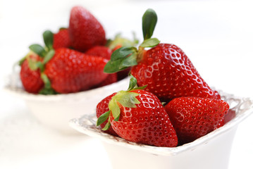 Fresh strawberries in the small ceramic bowls on the white table