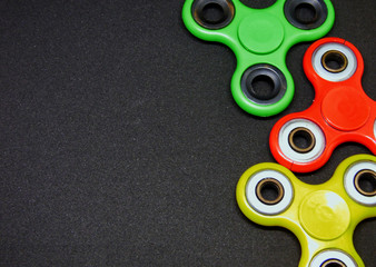 Bright colored fidget finger spinners on dark background. Red, green and yellow stress relieving toys. Selected focus. With empty space for text at the left.