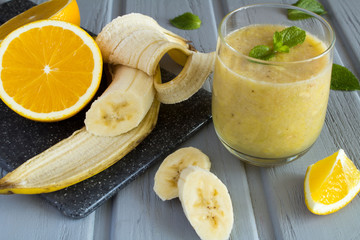 Smoothie and sliced banana and orange on the grey wooden background 