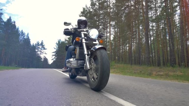 A low view on a motorcyclist riding a paved forest road.