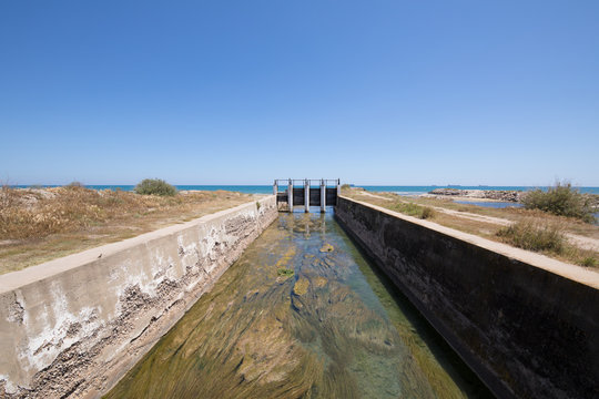 canal waterway river towards Mediterranean Sea with open ancient sluices, next to Gurugu Beach in Castellon, Valencia, Spain, Europe. Blue clear sky
