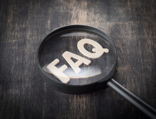 Magnifying glass on wood letters as FAQ abbreviation, frequently asked questions on wooden...