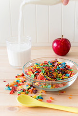 Kids healthy quick breakfast. Colorful rice cereal, flowing milk, apple on wooden background. Copy space