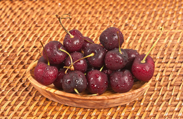 Macro of a hand, carved wood bowl of fresh, ripe, local cherries on a woven reed, place mat
