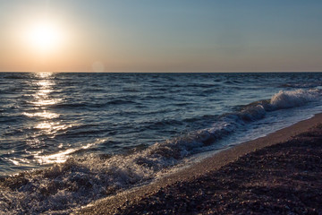 Sea waves at sunset at the shore with seashells. Beautiful background.