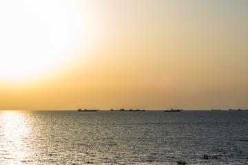 Naklejka na ściany i meble Sea beach with cargo ships on the horizon during sunset.