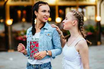 Portrait of two hipster girls friends with braids talking about something over city light background. Best friends