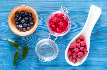 Homemade natural jam in glass jar and berries on blue wooden and canvas background top view