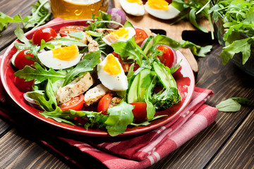 Fresh salad with chicken, tomatoes, eggs and arugula on plate
