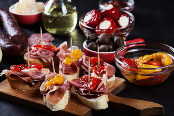 Spanish tapas with slices jamon serrano and grilled pepper. Also olives, salami, pickled onions, and peppers stuffed with cheese