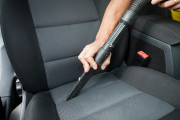 Young man hands vacuuming seat in car of the dust