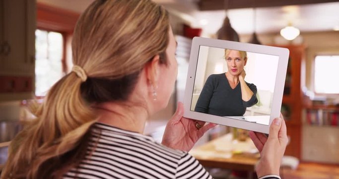 Woman having video chat with woman on tablet inside kitchen