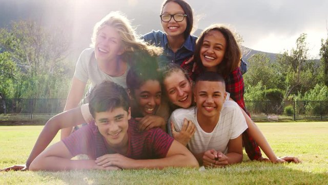 Group of teenage friends having fun lying in a pile on grass