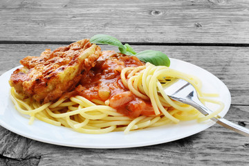 Schnitzel with spaghetti, tomato sauce and basil on wooden table - Piccata milanese