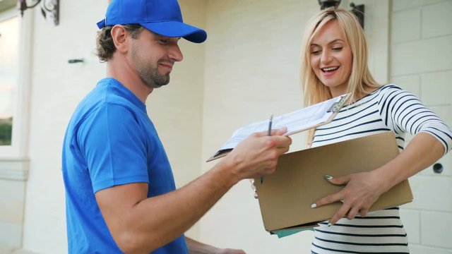 Courier delivering the cardboard to the house, happy woman receiving the package and signing the documents for getting this.