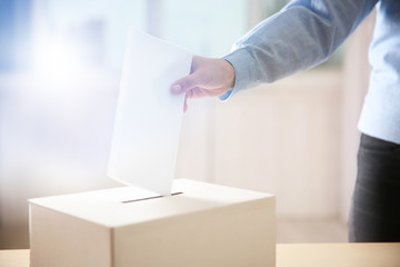 Closeup of hand inserting envelope in ballot box