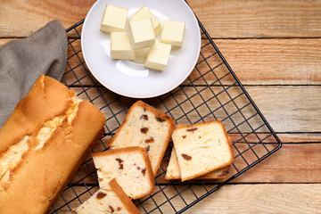 Cooling rack with delicious cake and plate of butter on wooden table
