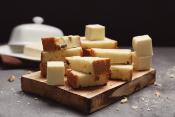 Cutting board with delicious sliced cake and cubes of butter on table