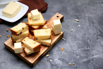 Cutting board with delicious sliced cake and cubes of butter on grey table