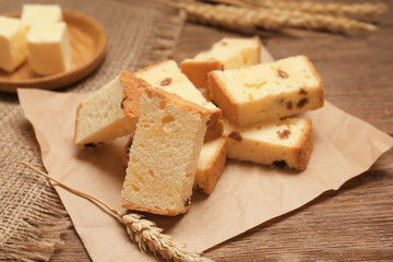 Paper with delicious butter cake and wheat ear on wooden table