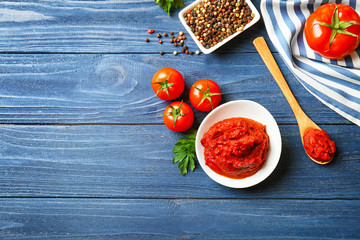 Ceramic bowl with sauce, spoon, tomatoes and spices on wooden table