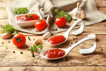 Ceramic spoons with tomato sauce and spices on wooden table