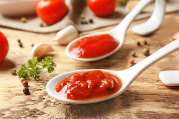 Ceramic spoons with tomato sauce and spices on wooden table