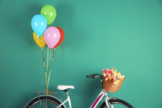 Fototapeta Bicycle with basket of flowers and balloons on color background