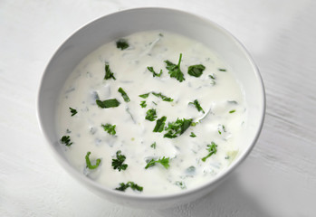 Bowl with delicious sauce and herbs on white wooden background, closeup