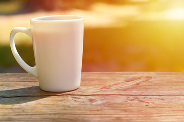 white mug with coffee stands on a wooden background. The concept of am and wake-up, sunlight