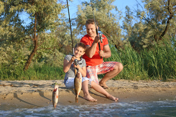 Fototapeta na wymiar Dad and son fishing from shore on river