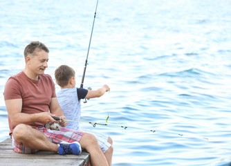 Dad and son fishing from pier on river