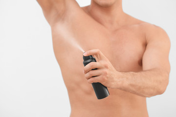 Handsome young man using deodorant on light background