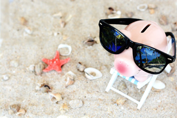 Savings for a holiday concept with piggy bank with sunglasses in a beach chair