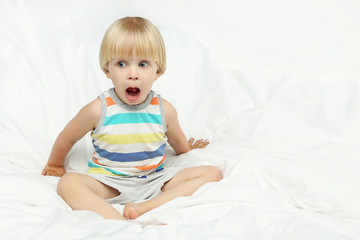 Little boy with open mouth sitting in white bed