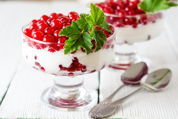 Yogurt dessert with red currant and decorated with leaves on white wooden background
