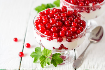 Yogurt dessert with red currant and decorated with leaves on white wooden background