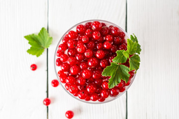 Yogurt dessert with red currant and decorated with leaves on white wooden background