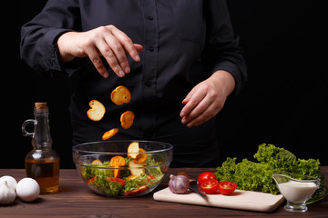 Chef dropping croutons to a bowl with caesar salad, cooking process, restaurant concept