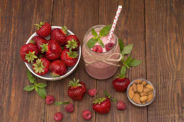Pink strawberry and raspberry smoothie in a mason jar glass with straw and scattered berries