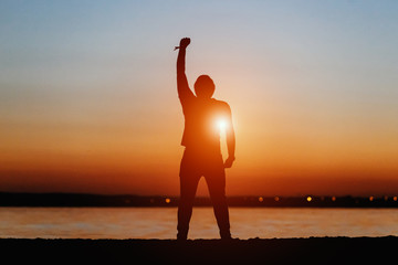 Young happy man at sunset, silhouette of rock star pose