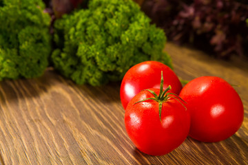 Fresh ripe tomatoes on a wooden table with a green salad on the background. Fresh vegetables.
