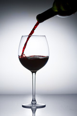 Pouring red wine from bottle to glass on gray